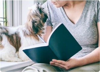 Donna con un libro in mano mentre guarda il cane accanto a lei.